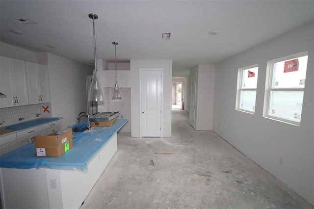 kitchen featuring hanging light fixtures, white cabinetry, backsplash, and concrete flooring