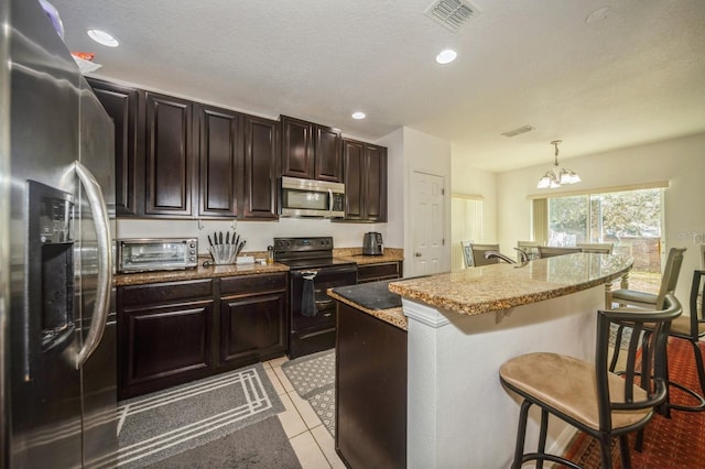 kitchen featuring a kitchen breakfast bar, a chandelier, decorative light fixtures, a center island with sink, and appliances with stainless steel finishes