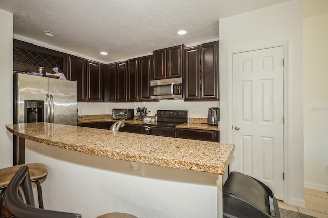 kitchen with a kitchen breakfast bar, light tile patterned floors, light stone countertops, and appliances with stainless steel finishes