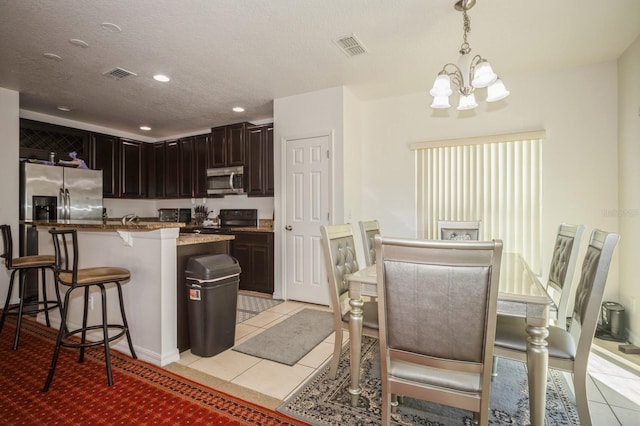 kitchen featuring appliances with stainless steel finishes, light tile patterned floors, a chandelier, hanging light fixtures, and a breakfast bar area