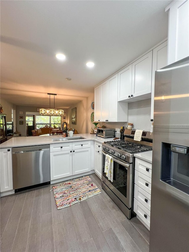 kitchen with sink, light wood-type flooring, appliances with stainless steel finishes, decorative light fixtures, and kitchen peninsula