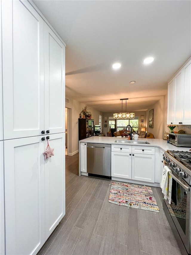 kitchen featuring kitchen peninsula, hanging light fixtures, light hardwood / wood-style flooring, white cabinetry, and stainless steel appliances