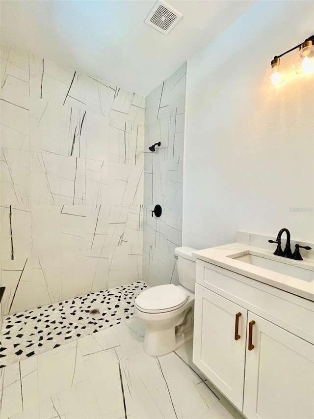 bathroom with tiled shower, vanity, and toilet