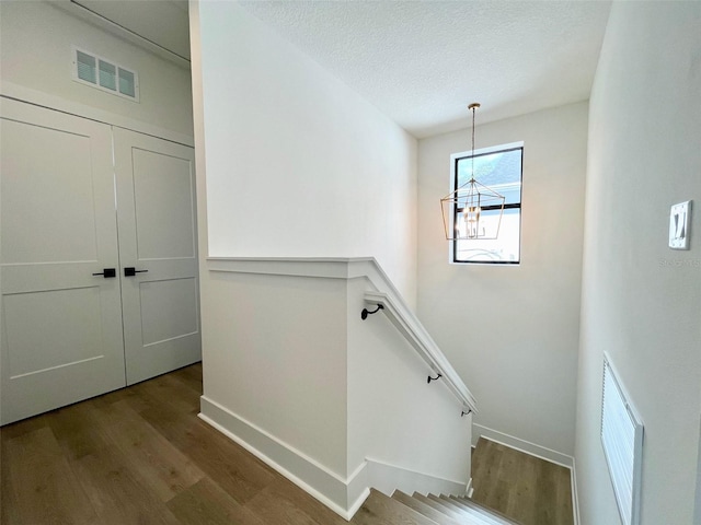 stairway with a notable chandelier, a textured ceiling, and hardwood / wood-style flooring