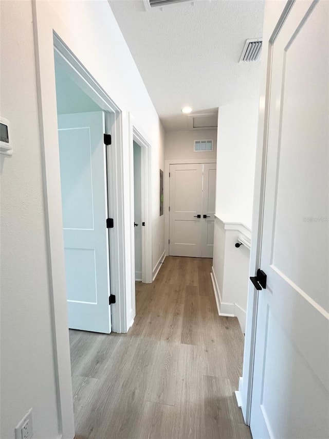 hall featuring a textured ceiling and light hardwood / wood-style flooring