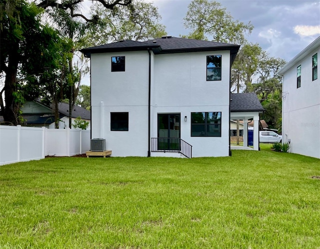 rear view of house with central AC and a lawn