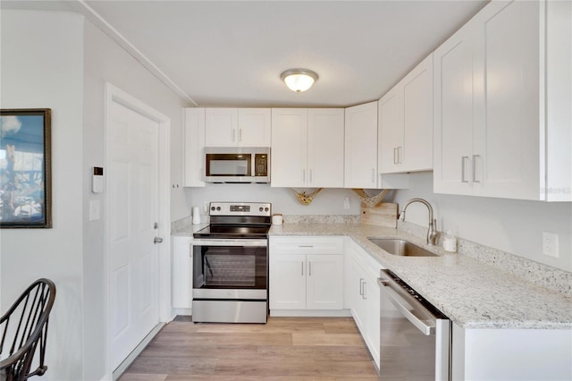 kitchen with light stone counters, stainless steel appliances, sink, white cabinets, and light hardwood / wood-style floors