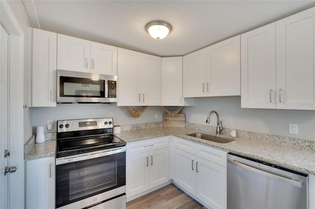 kitchen featuring light stone countertops, sink, stainless steel appliances, light hardwood / wood-style flooring, and white cabinets