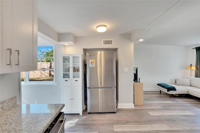 kitchen featuring light hardwood / wood-style floors, light stone countertops, white cabinetry, and appliances with stainless steel finishes