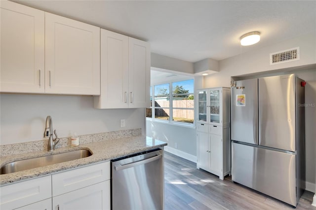 kitchen featuring stainless steel appliances, white cabinetry, light hardwood / wood-style floors, and light stone counters