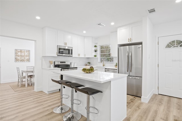 kitchen featuring stainless steel appliances, a kitchen island, white cabinetry, and light hardwood / wood-style floors