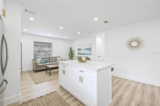 kitchen featuring stainless steel fridge, a kitchen island, light wood-type flooring, and white cabinetry