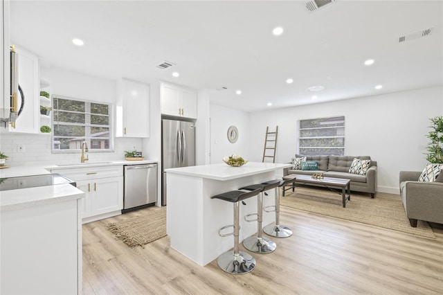 kitchen featuring white cabinets, light hardwood / wood-style floors, backsplash, and appliances with stainless steel finishes