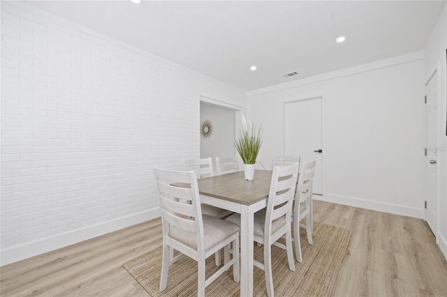 dining room with light hardwood / wood-style flooring, crown molding, and brick wall