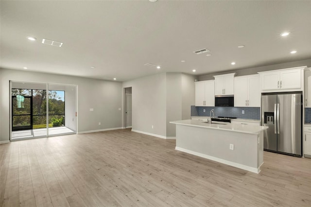 kitchen with sink, white cabinets, stainless steel fridge, a center island with sink, and light wood-type flooring