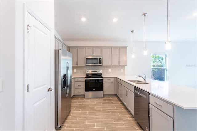 kitchen with sink, light wood-type flooring, decorative light fixtures, kitchen peninsula, and stainless steel appliances