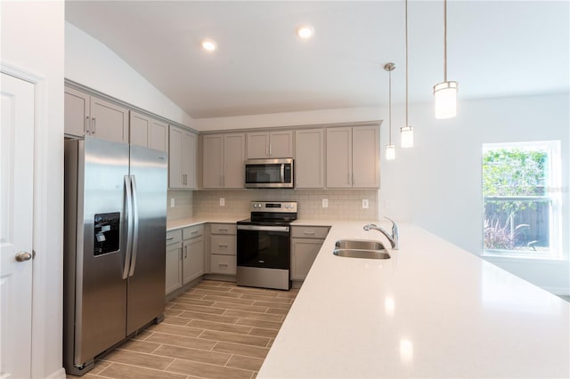 kitchen with appliances with stainless steel finishes, vaulted ceiling, sink, light hardwood / wood-style floors, and hanging light fixtures