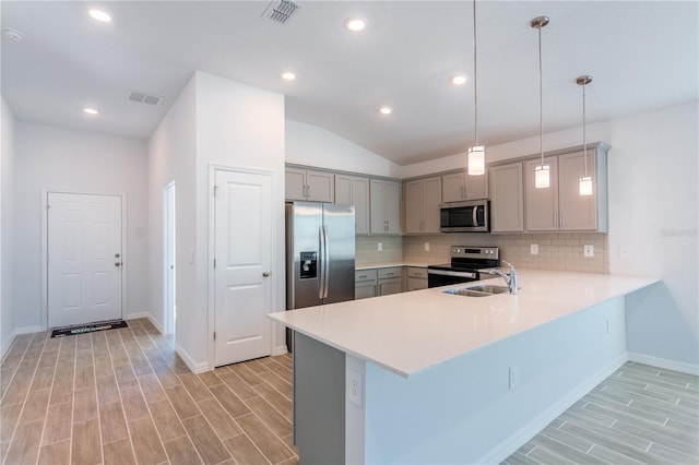 kitchen with kitchen peninsula, light wood-type flooring, stainless steel appliances, vaulted ceiling, and pendant lighting