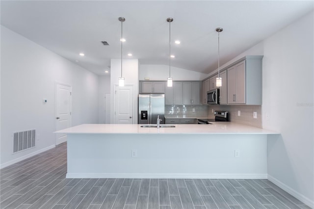 kitchen with lofted ceiling, hanging light fixtures, hardwood / wood-style flooring, appliances with stainless steel finishes, and kitchen peninsula