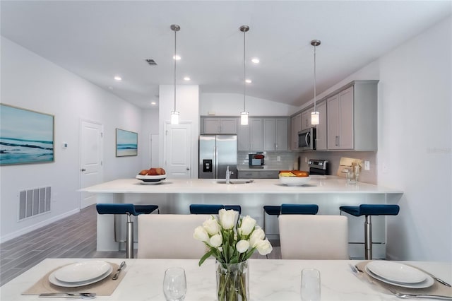 kitchen featuring appliances with stainless steel finishes, tasteful backsplash, gray cabinetry, vaulted ceiling, and hanging light fixtures