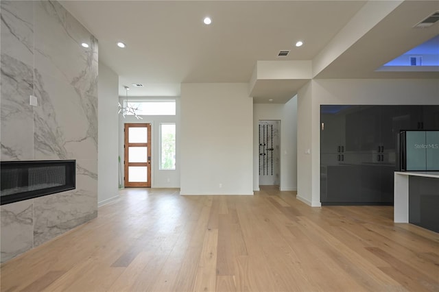 unfurnished living room with light hardwood / wood-style floors, a fireplace, and an inviting chandelier