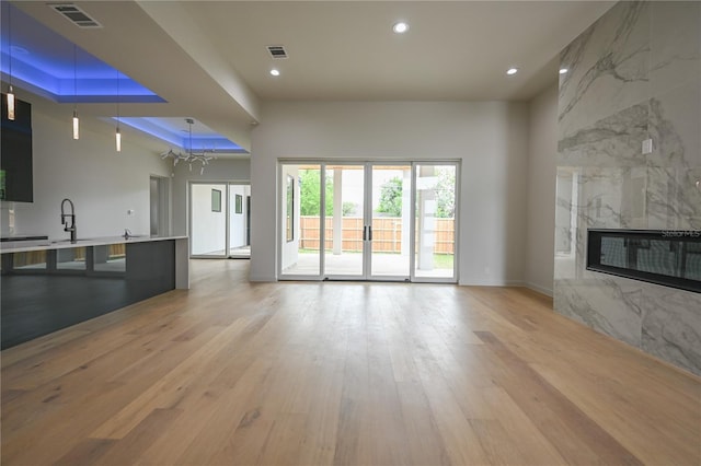 unfurnished living room with a high end fireplace, light wood-type flooring, a tray ceiling, sink, and a notable chandelier