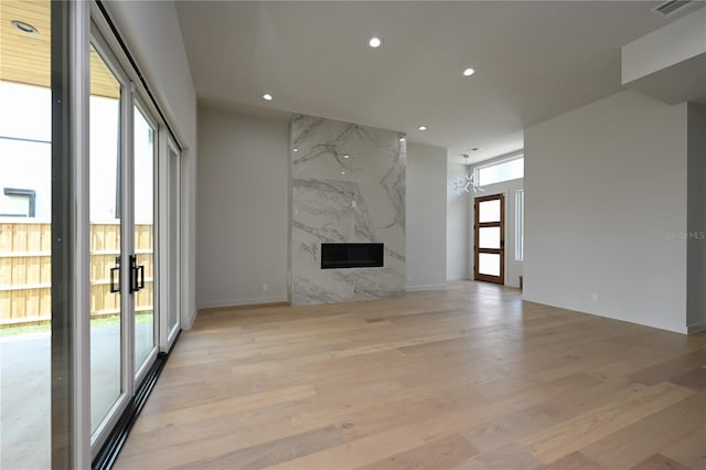 unfurnished living room with light hardwood / wood-style flooring, a high end fireplace, and an inviting chandelier