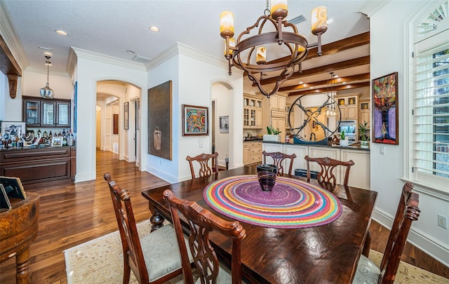 dining space with dark hardwood / wood-style flooring, a textured ceiling, bar area, ornamental molding, and a chandelier