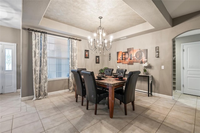 tiled dining area with a raised ceiling, a textured ceiling, and a chandelier