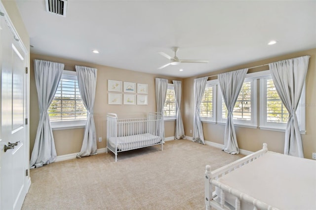 carpeted bedroom featuring ceiling fan and a nursery area