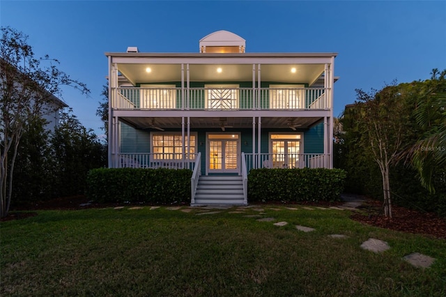 back house at dusk featuring french doors, a yard, and a porch