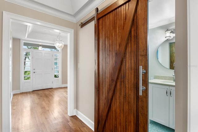 entryway with crown molding, a barn door, wood finished floors, and baseboards