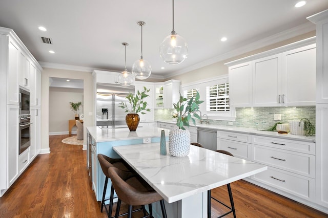 kitchen featuring a breakfast bar area, hanging light fixtures, white cabinets, a kitchen island, and built in appliances