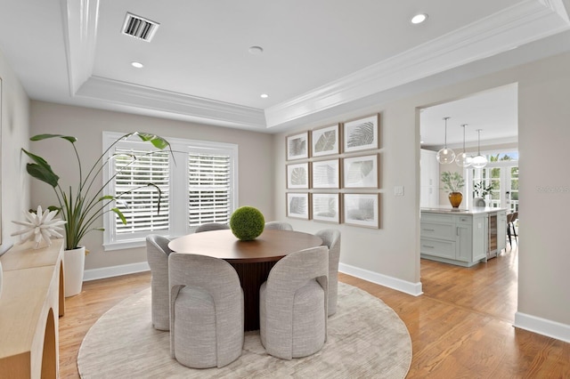 dining area featuring a tray ceiling, visible vents, crown molding, and light wood finished floors