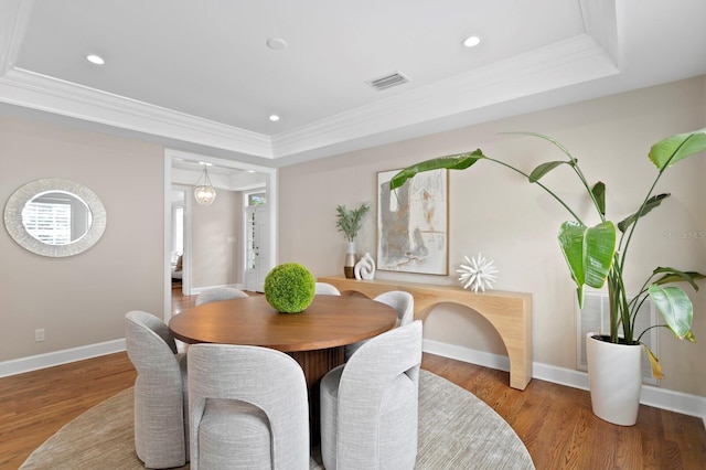 dining area with crown molding, visible vents, a raised ceiling, and wood finished floors