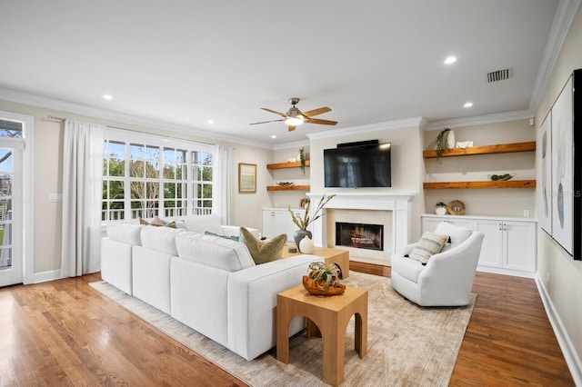 living room featuring ornamental molding, light wood-style flooring, a high end fireplace, and visible vents