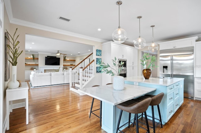 kitchen featuring hanging light fixtures, appliances with stainless steel finishes, white cabinetry, a kitchen island, and a kitchen breakfast bar