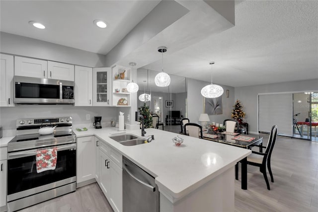 kitchen featuring white cabinets, sink, light wood-type flooring, kitchen peninsula, and stainless steel appliances