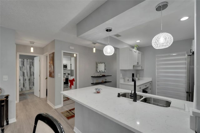 kitchen featuring stainless steel appliances, sink, decorative light fixtures, white cabinets, and light hardwood / wood-style floors