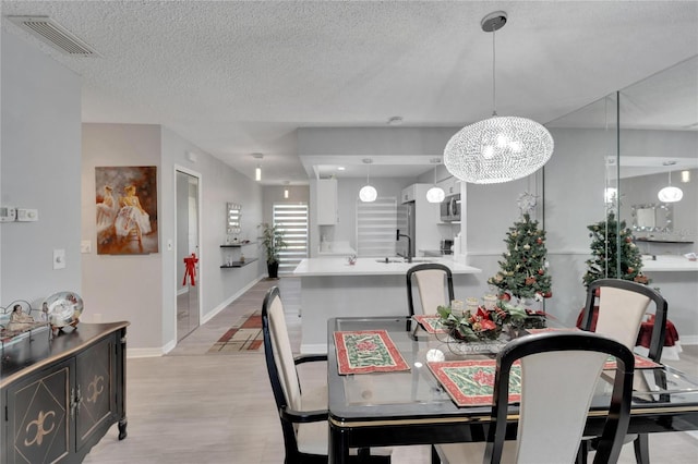 dining space featuring a textured ceiling, sink, light hardwood / wood-style flooring, and a chandelier