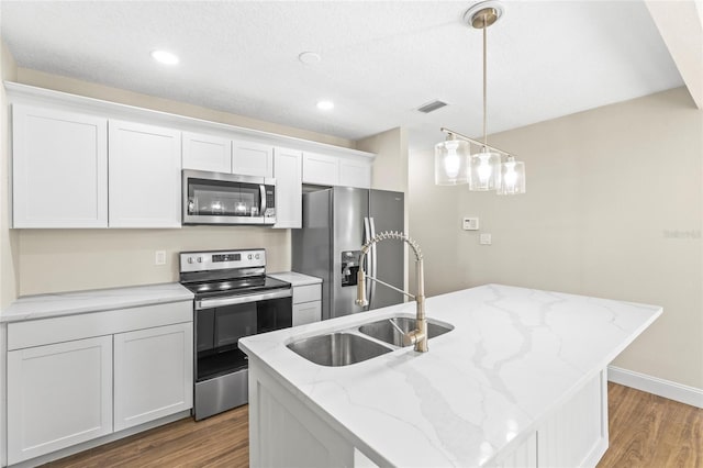 kitchen with pendant lighting, appliances with stainless steel finishes, white cabinetry, wood-type flooring, and an island with sink