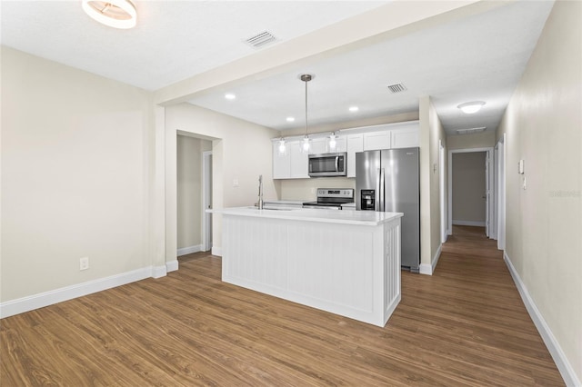 kitchen with white cabinets, hanging light fixtures, appliances with stainless steel finishes, and an island with sink