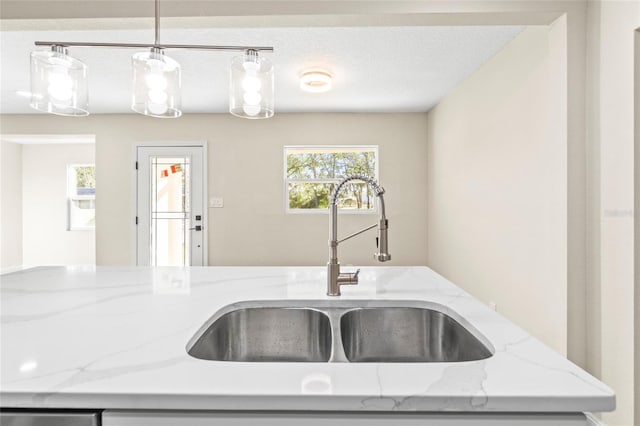 kitchen featuring a textured ceiling, decorative light fixtures, sink, and light stone countertops