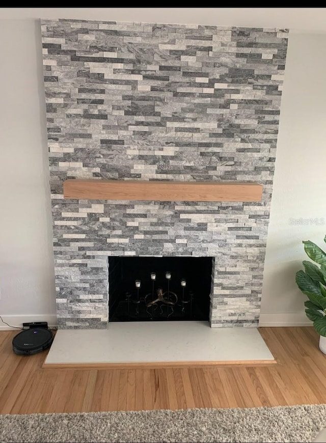 details with a stone fireplace, wood finished floors, and baseboards