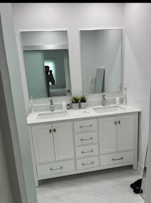 full bath with double vanity, marble finish floor, a sink, and a textured wall