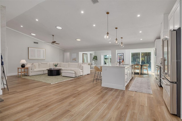 kitchen featuring hanging light fixtures, light hardwood / wood-style flooring, an island with sink, white cabinetry, and stainless steel appliances