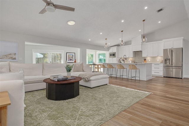 living room with ceiling fan, plenty of natural light, vaulted ceiling, and light hardwood / wood-style flooring