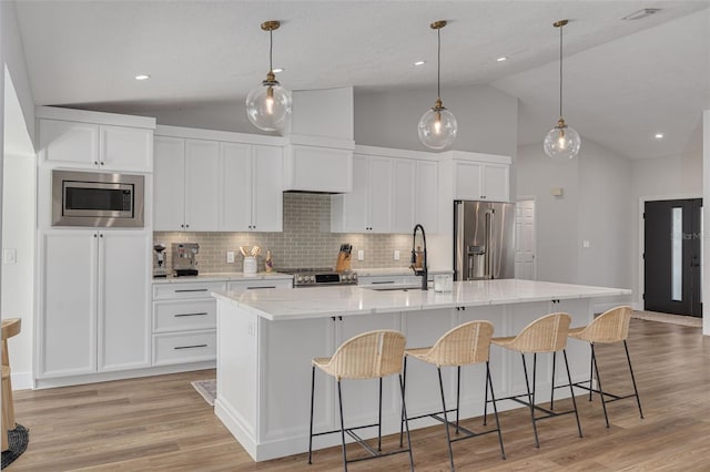 kitchen featuring sink, stainless steel appliances, light hardwood / wood-style flooring, pendant lighting, and a center island with sink