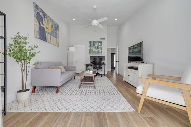 living room featuring ceiling fan, light wood-type flooring, and a towering ceiling