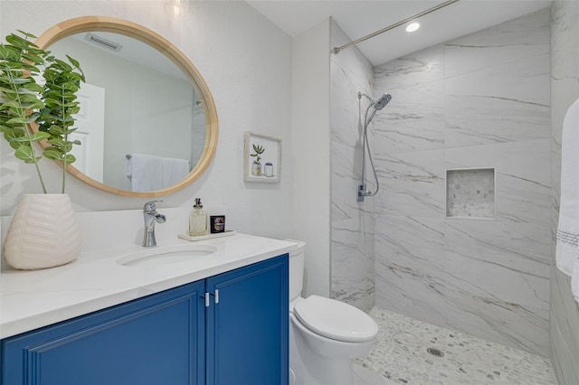 bathroom with a tile shower, vanity, and toilet